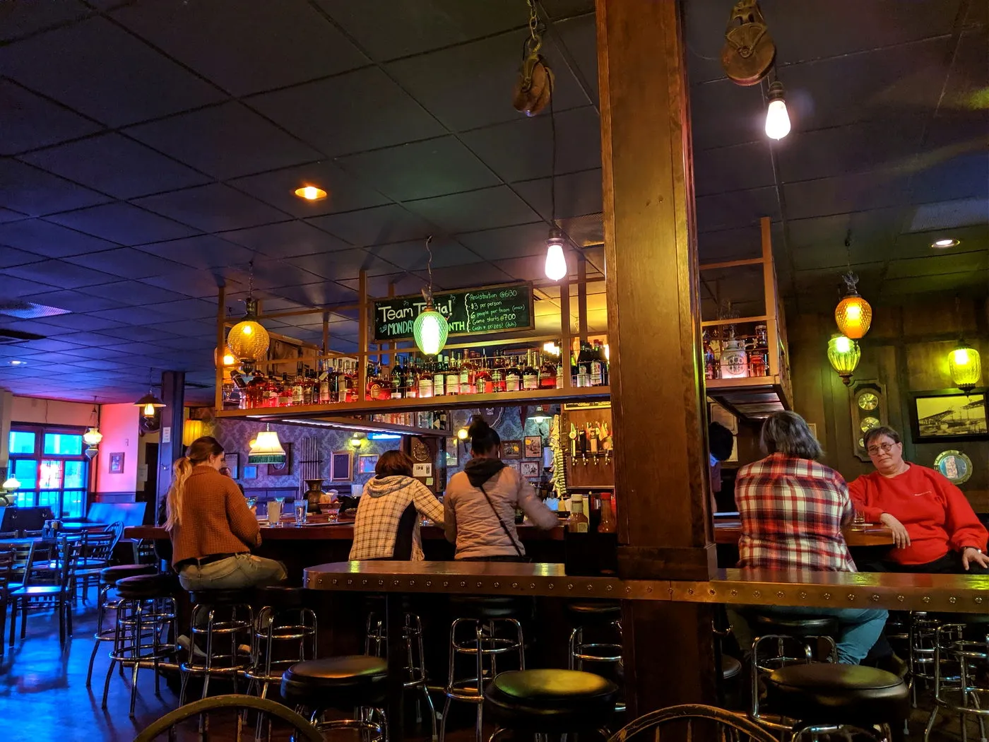 Regulars along the bar at night under colored glass pendant lamps
