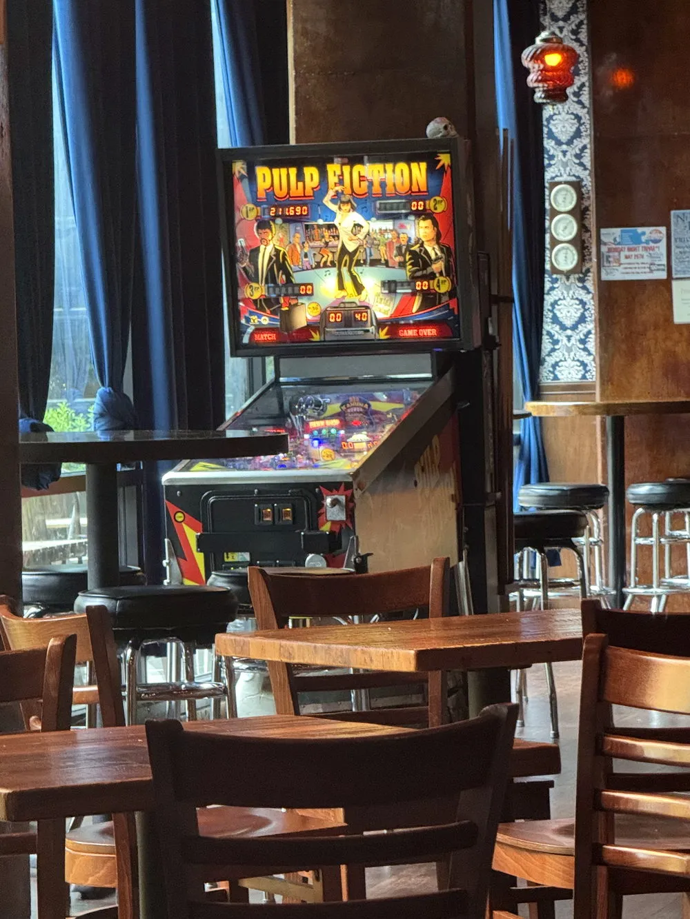 Pinball machine beside the blue curtains and damask wall