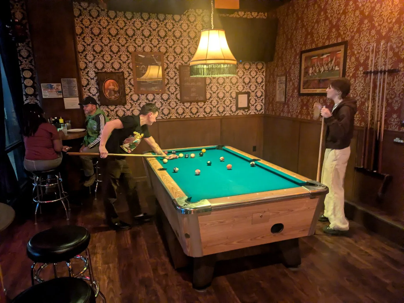 Players at the pool table in the back room, surrounded by red and gold damask wallpaper