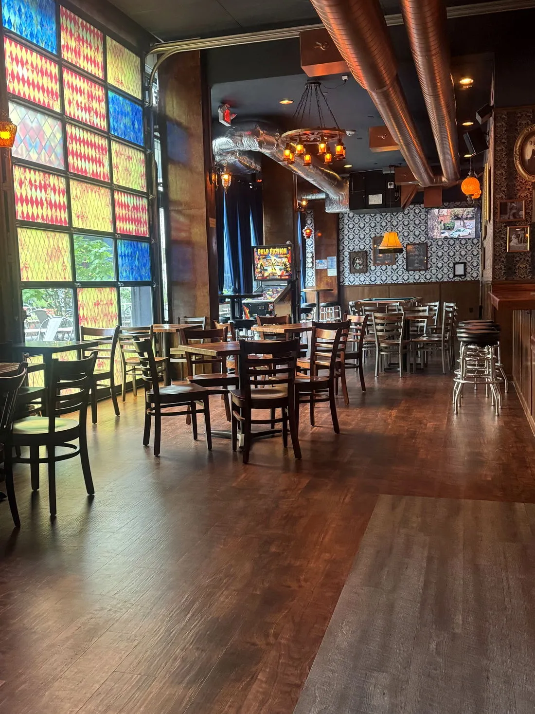 The front room with tall stained-glass harlequin windows and wooden tables